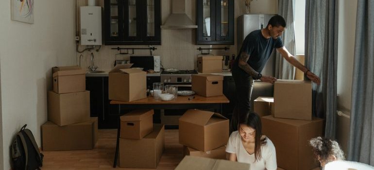 a man carrying a box while his wife and daughter are unpacking boxes in the floor of the kitchen