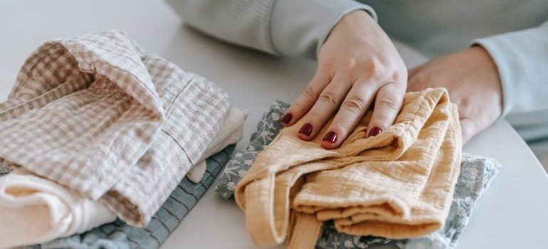 Woman's hands folding baby clothes on a bed.