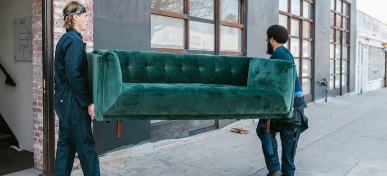 Two man carrying a green sofa. 