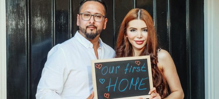 A couple holding "our first home" sign