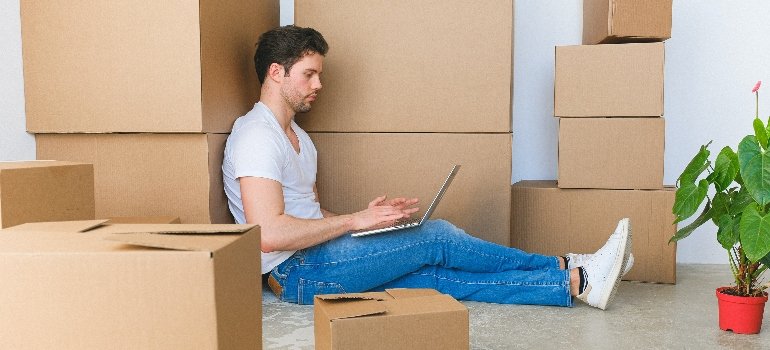a man sitting next to a pile of boxes using his laptop to read about portable storage vs. traditional moving companies 