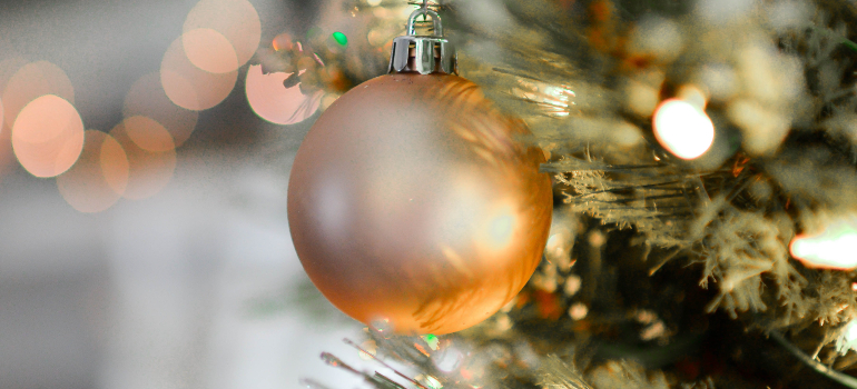 A close-up of a shiny copper-colored Christmas ball ornament hanging on the boughs of a festive tree.