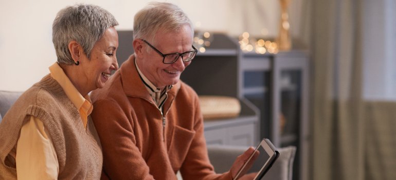 A senior couple sits comfortably at home, sharing a joyful moment as they browse through a tablet together.